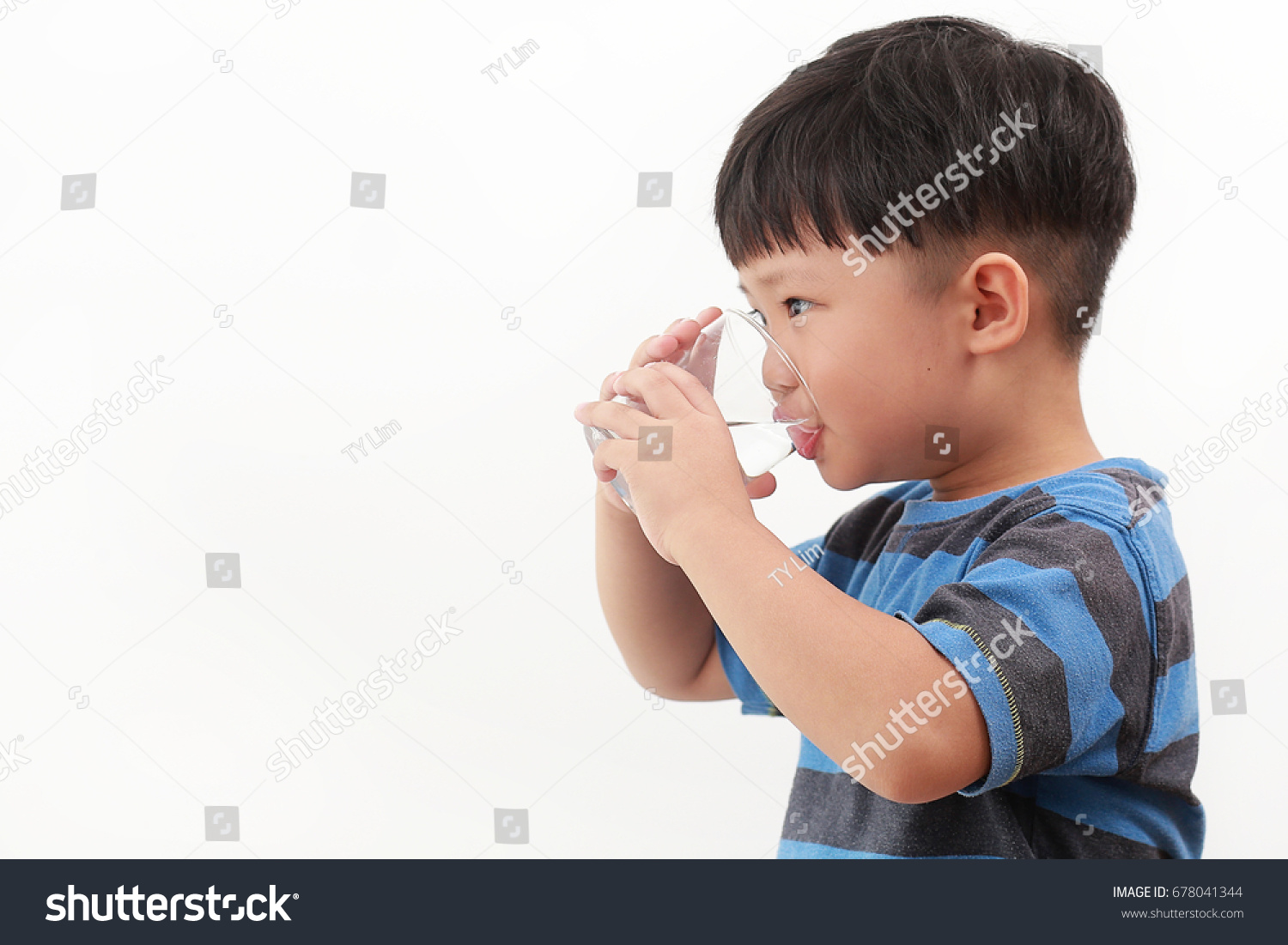 Cute little Asian boy drinking water from glass on white background