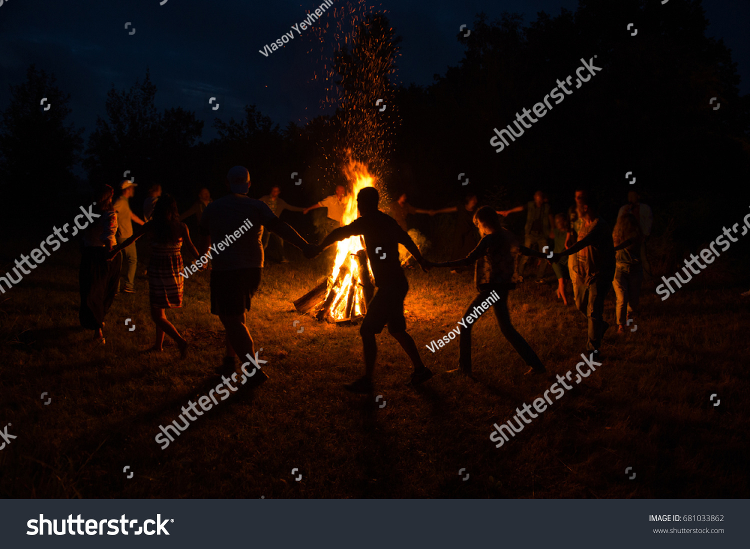People dance around the campfire. People dance around the fire at night.
