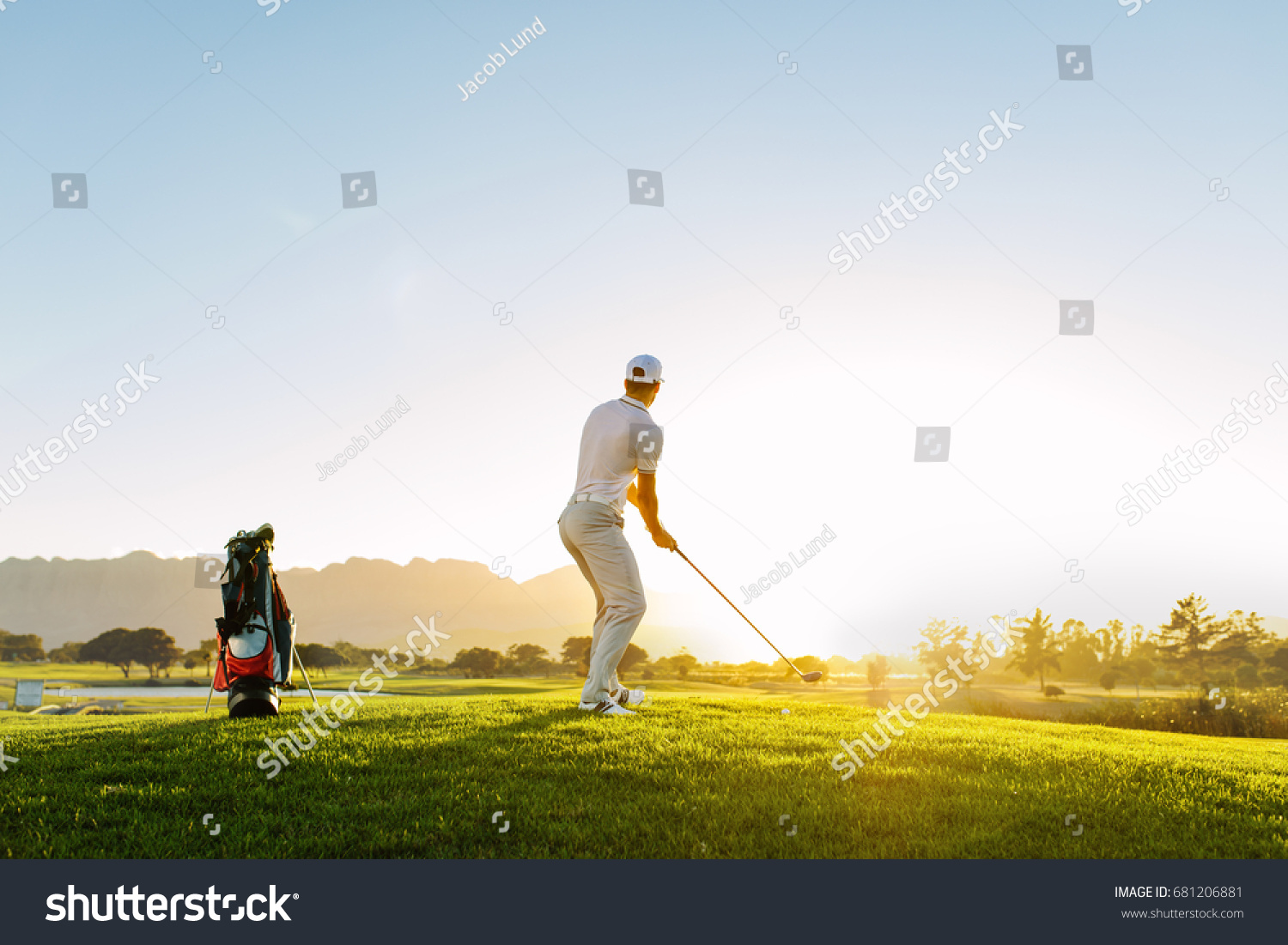 Full length of golf player playing golf on sunny day. Professional male golfer taking shot on golf course.