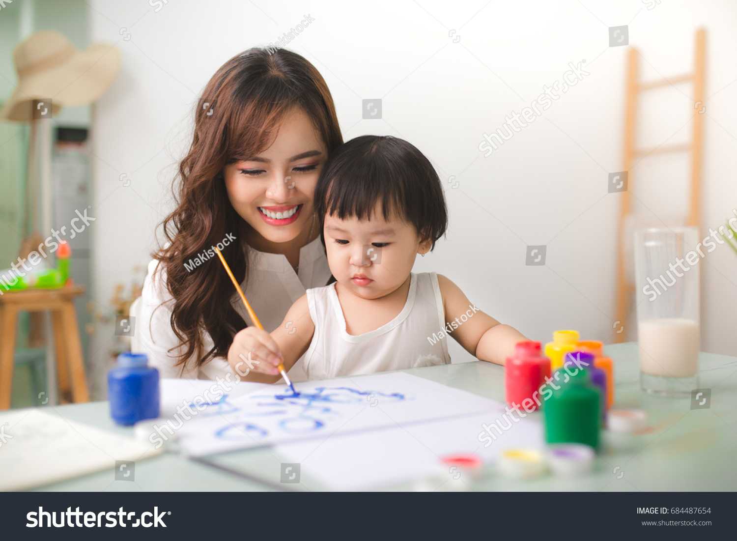 Happy family mother and daughter together paint. Asian woman helps her child girl.