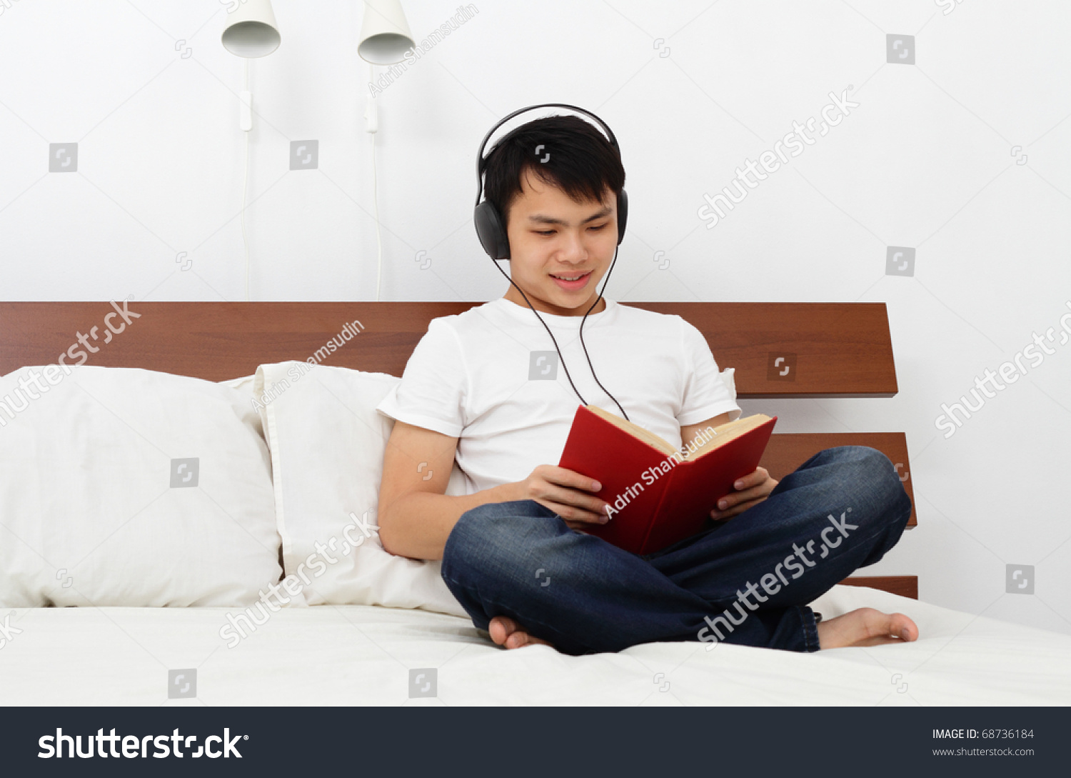 A young Asian man reading a book on a bed