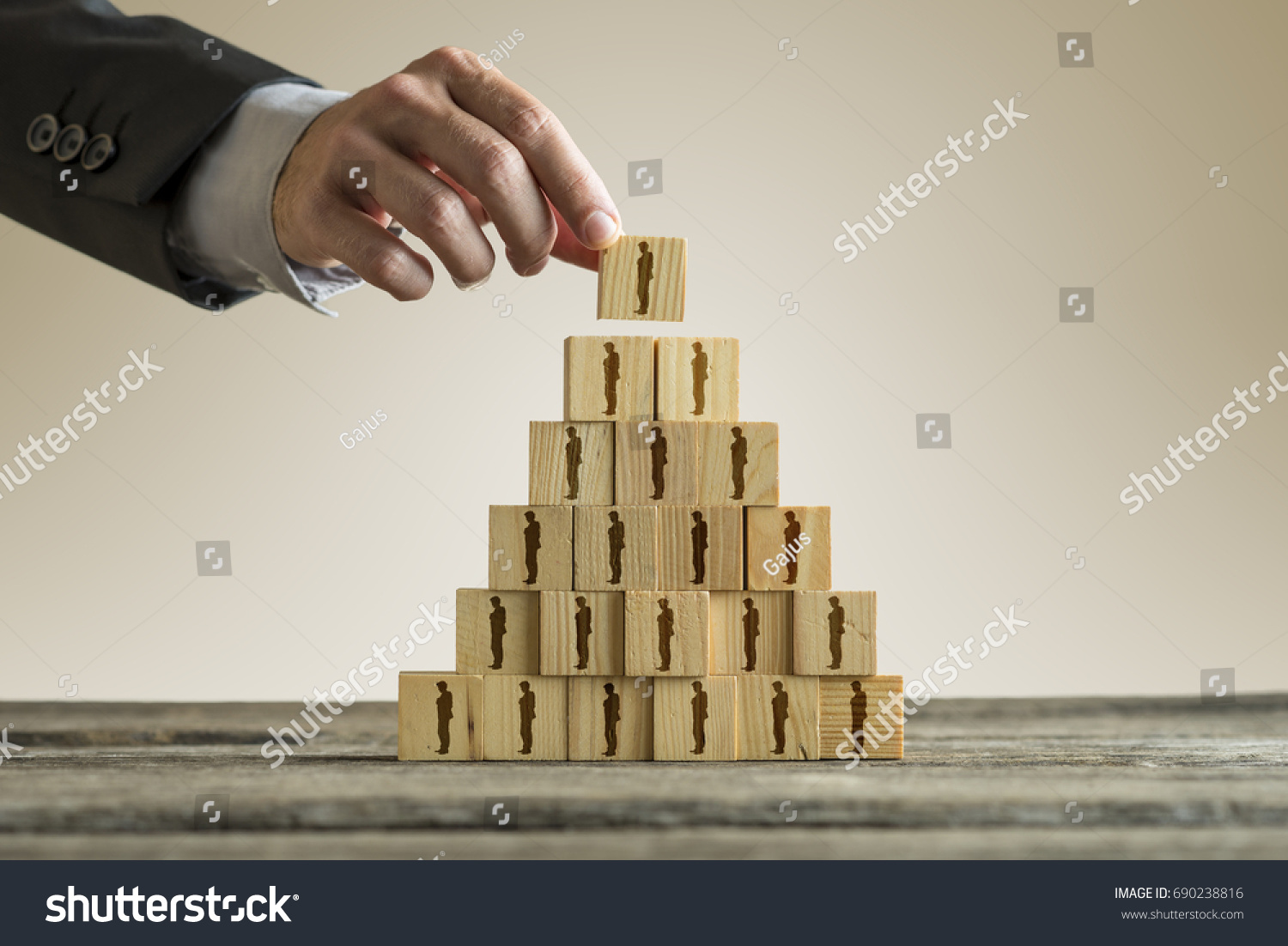 Businessman building a pyramid of wood blocks with people silhouettes  human resources and management concept.