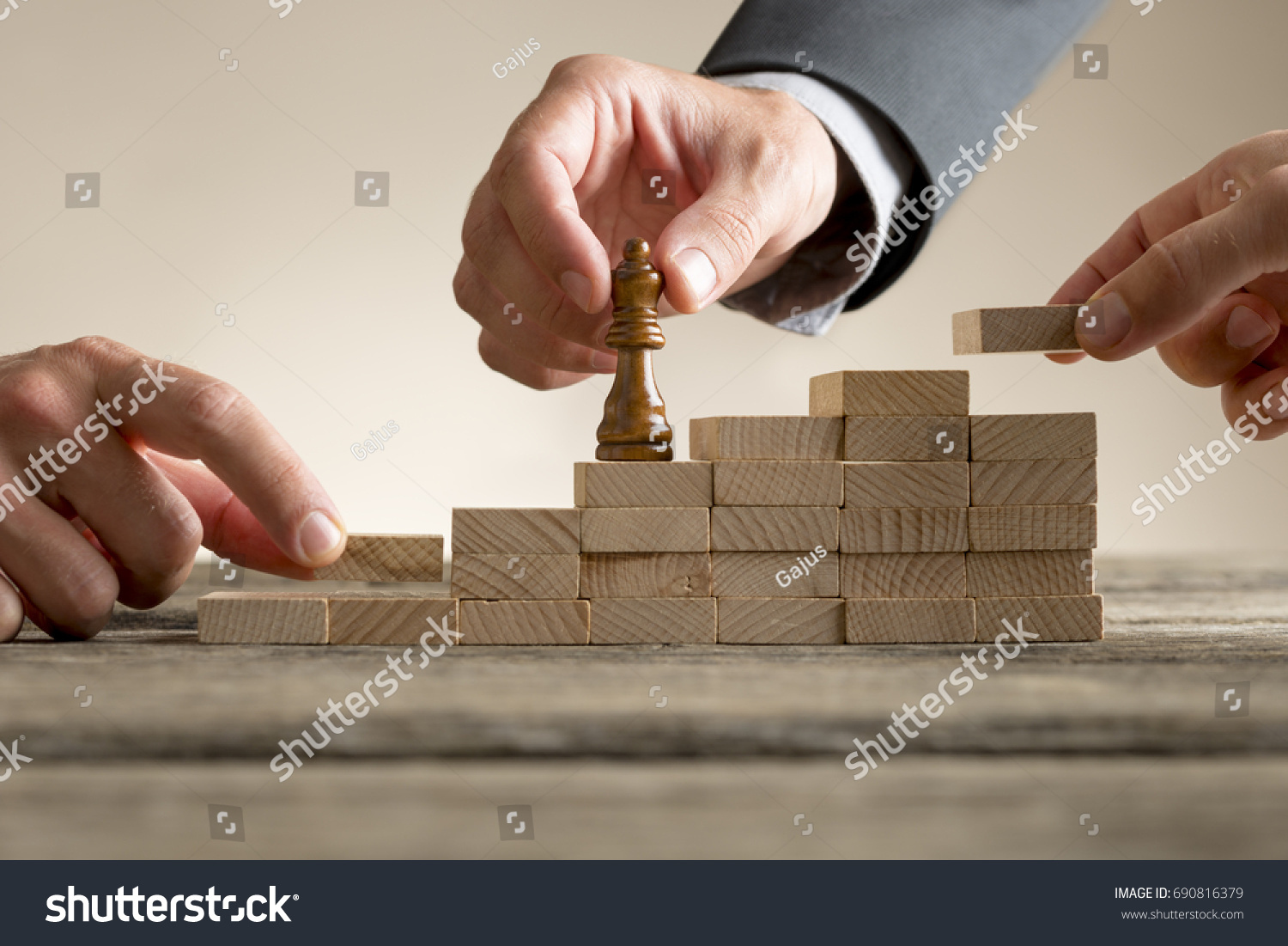 Business success and promotion concept with a businessman moving a chess piece up a series of steps formed by building blocks being put in place by his team in a close up view.