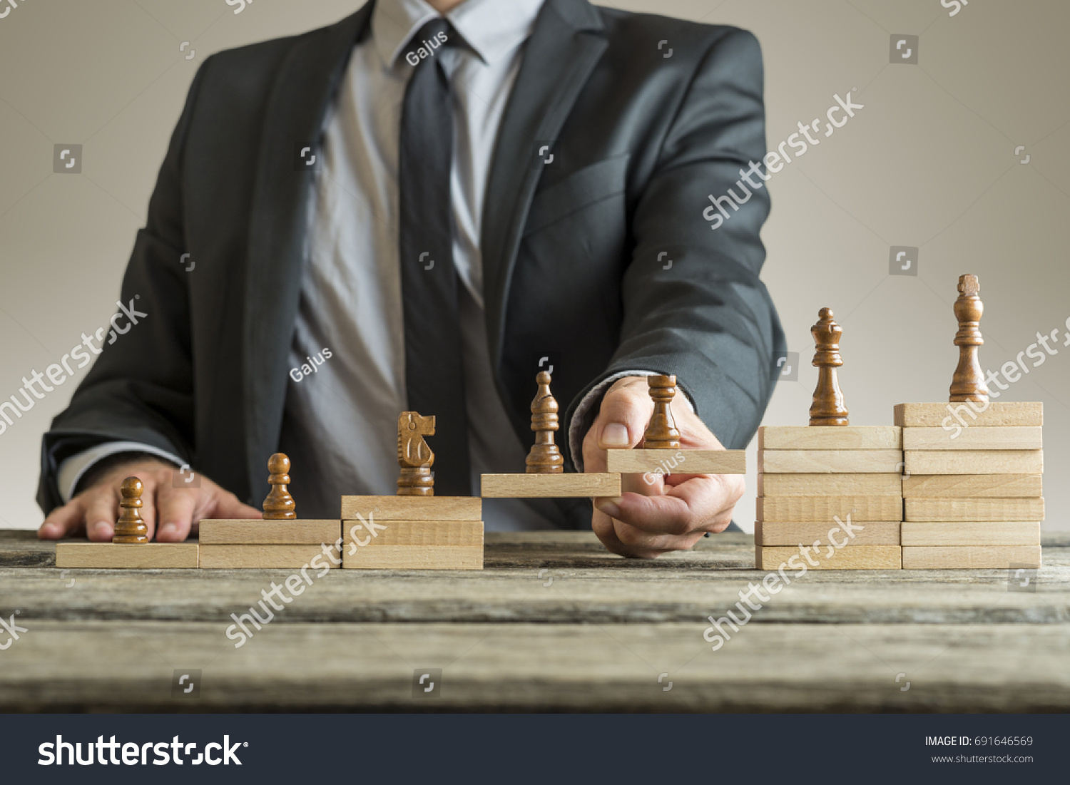 Conceptual image of career management with a businessman forming a bridge of wooden building blocks for chess pieces developing from pawn to king.