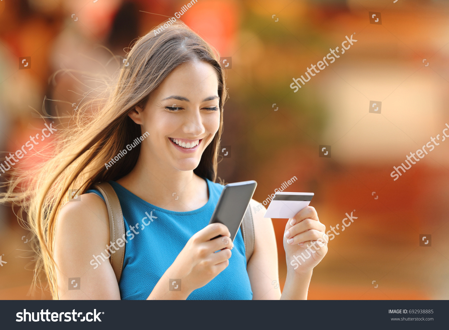 Happy shopper woman buying on line with a smart phone and a credit card on the street