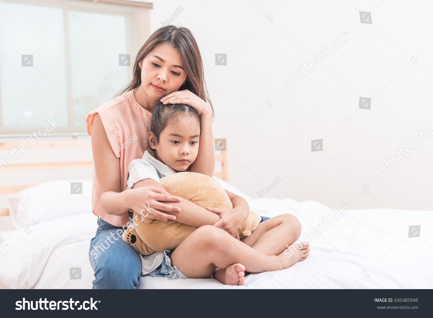 Asian mother hugging and comforting her sad daughter in bed room