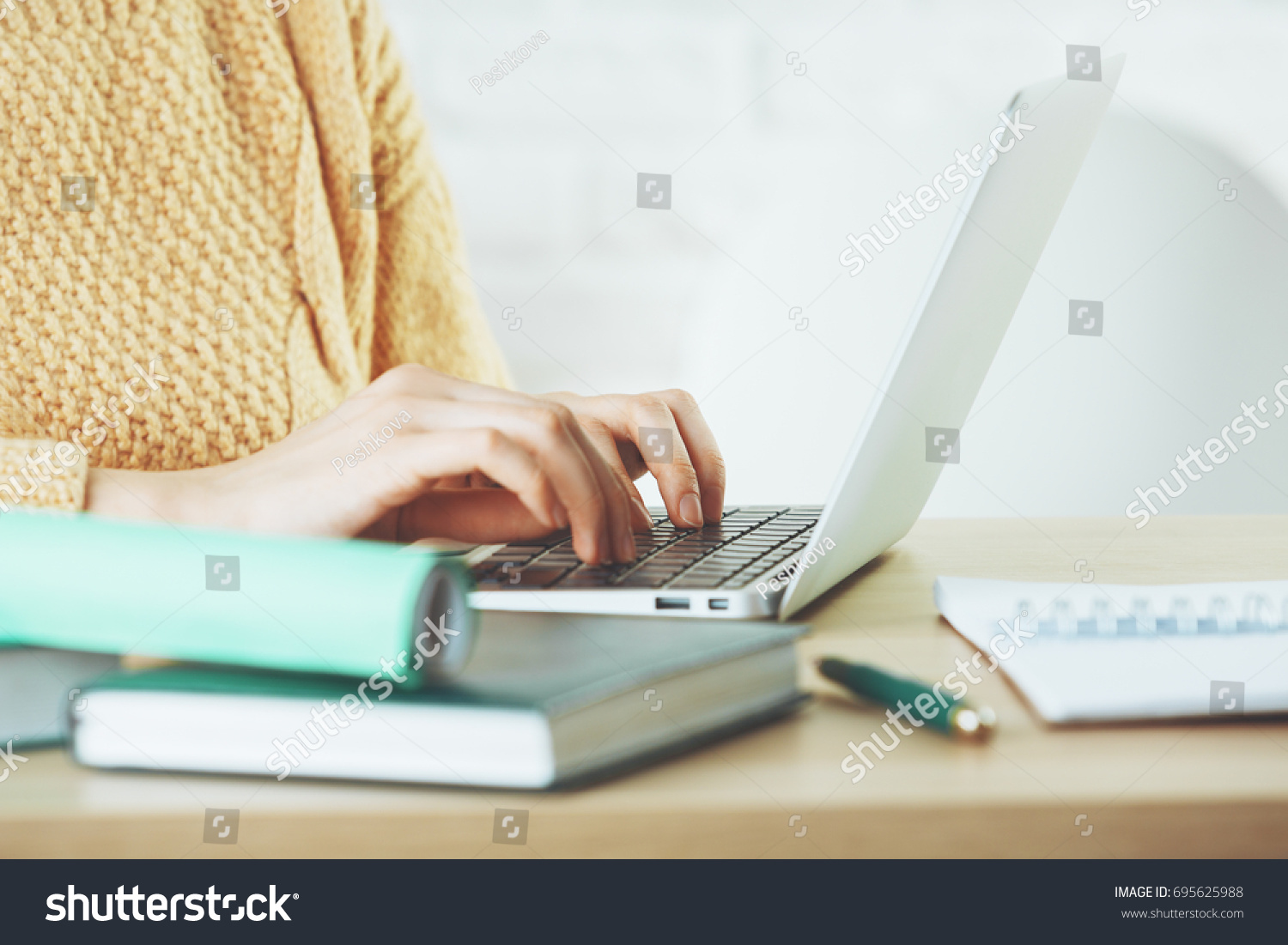 Side view and close up of woman hands typing on laptop keyboard placed on wooden office desktop with supplies. Technology concept