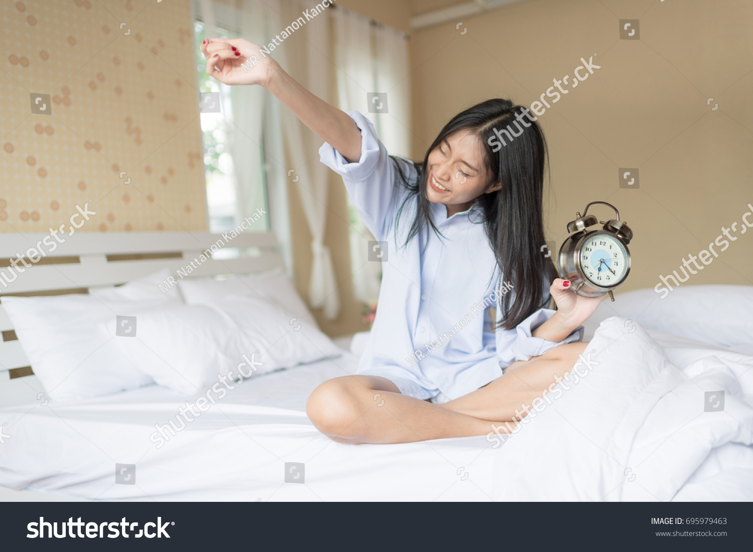 Wake up woman on bed with an ancient Copper Alarm clock in hand. Lazy woman.