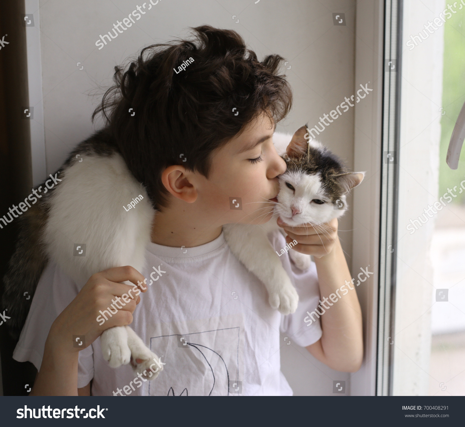 teenager boy with cat kissing look out of the window close up portriait
