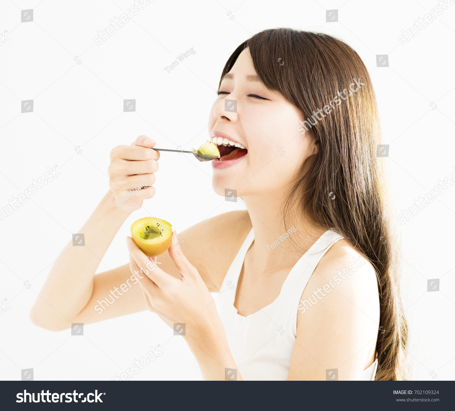 Happy young woman eating kiwi fruit