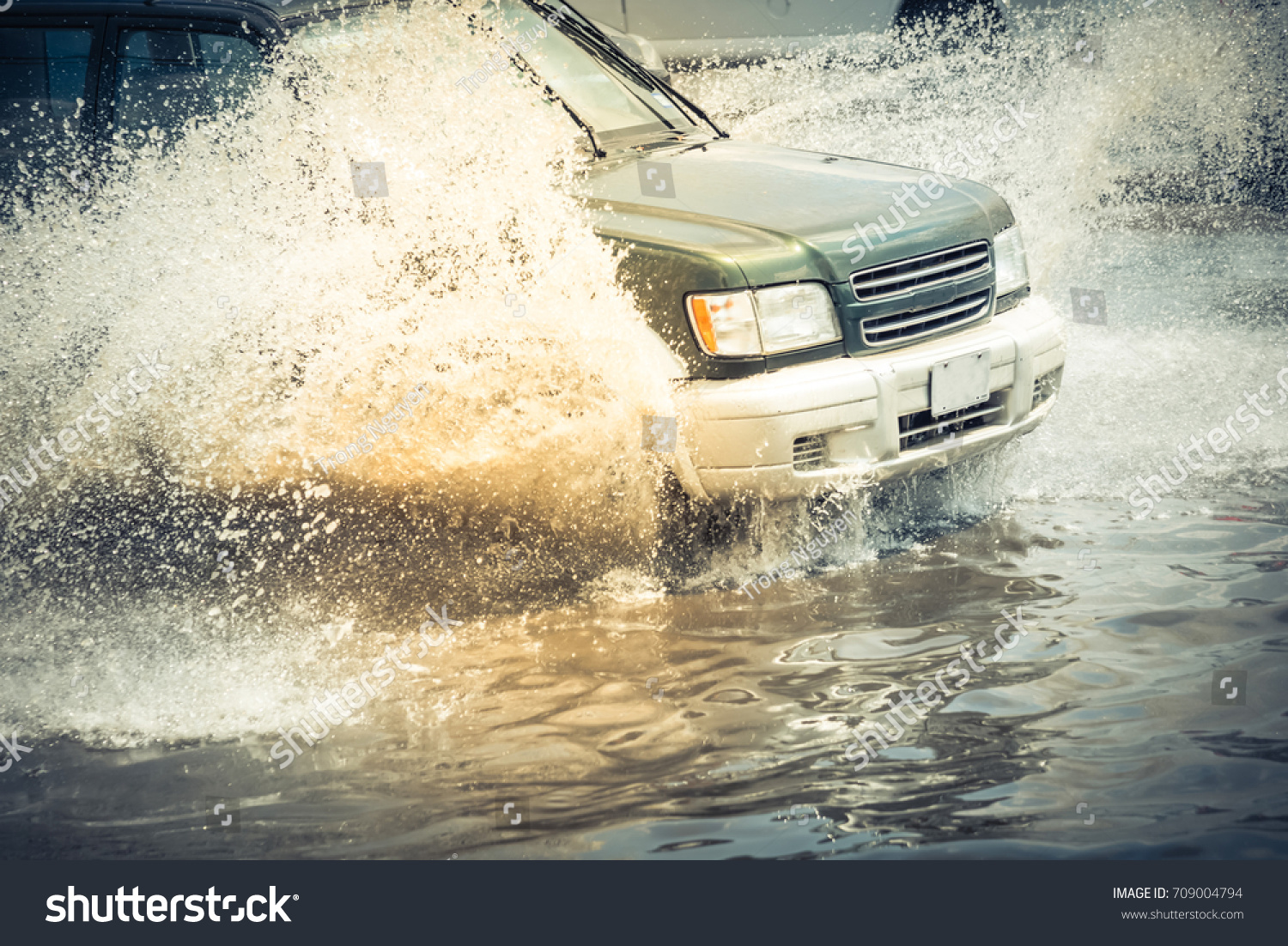Splash by car as it goes through flood water after heavy rains of Harvey hurricane storm in Houston Texas US. Flooded city road big puddle spray from the wheels of SUV car roaring by. Vintage tone