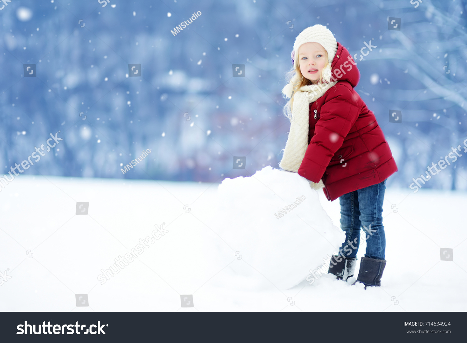 Adorable little girl building a snowman in beautiful winter park. Cute child playing in a snow. Winter activities for kids.