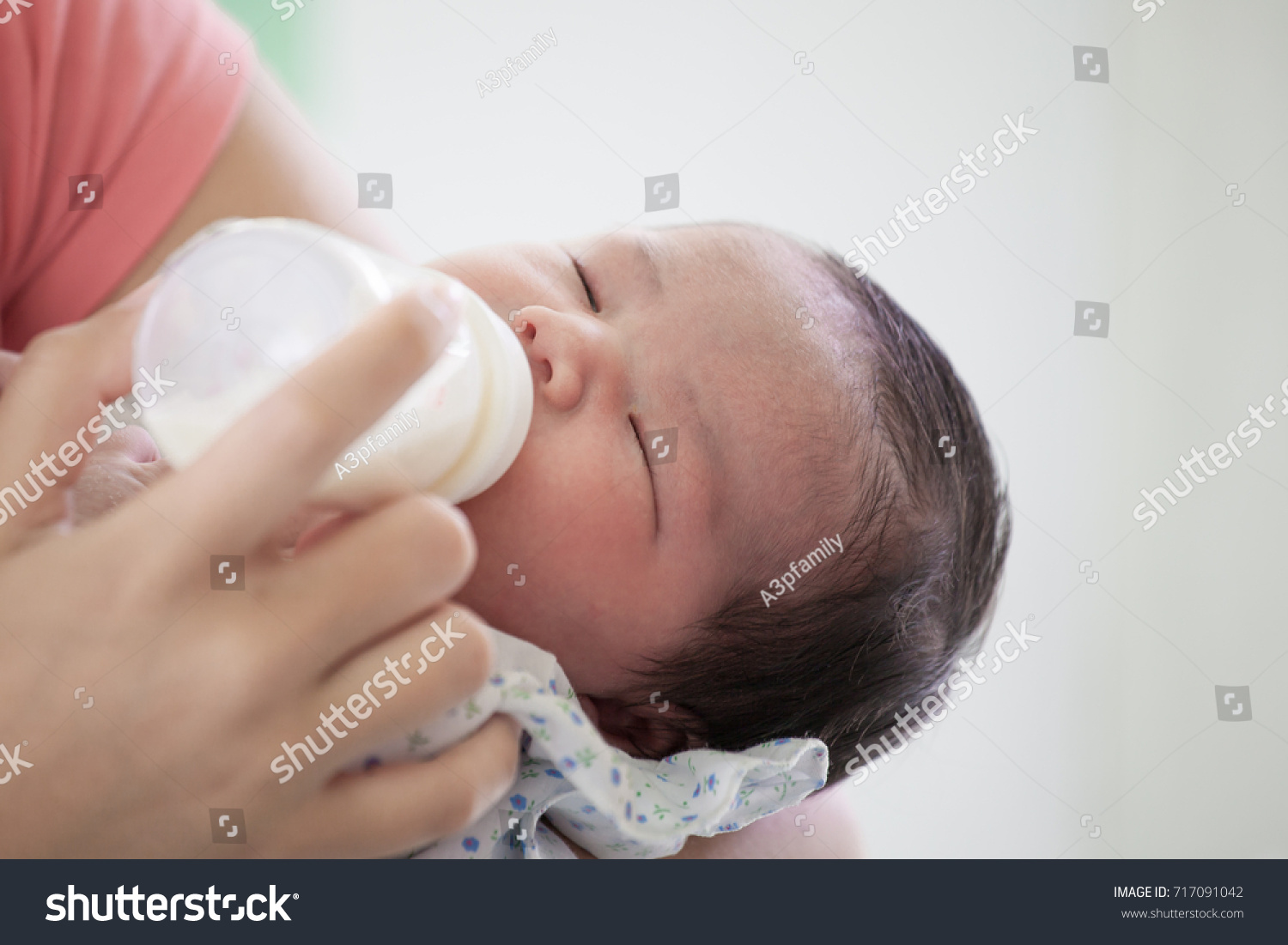 Sleeping newborn baby little girl drinking a milk from bottle in her mother's arms