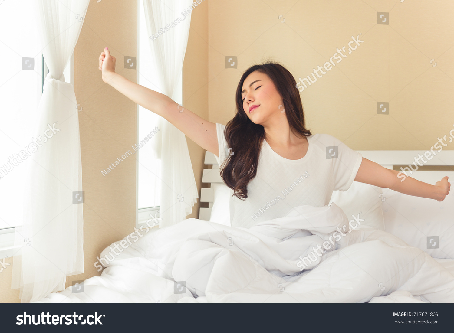 Asian woman wake up in the morning sitting on white bed and stretching feeling happy and fresh