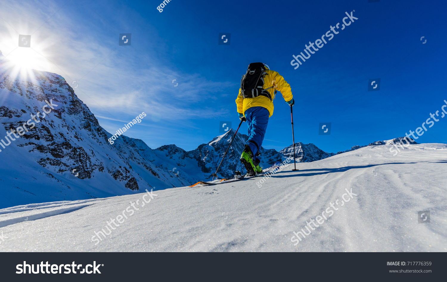 Mountaineer backcountry ski spring walking up along a snowy ridge with skis in the backpack. In background blue cloudy sky and shiny sun and Tre Cime  Drei Zinnen in South Tirol  Dolomites  Italy. 