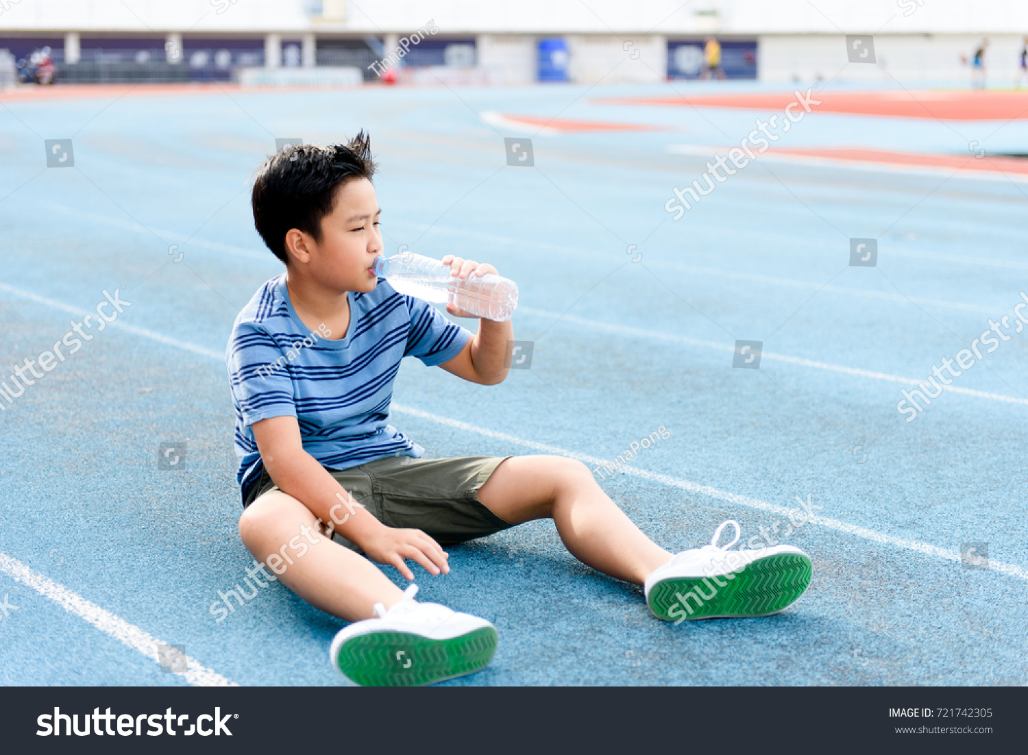 Young Asian Thai boy drinking water from bottle during resting on the blue track after running