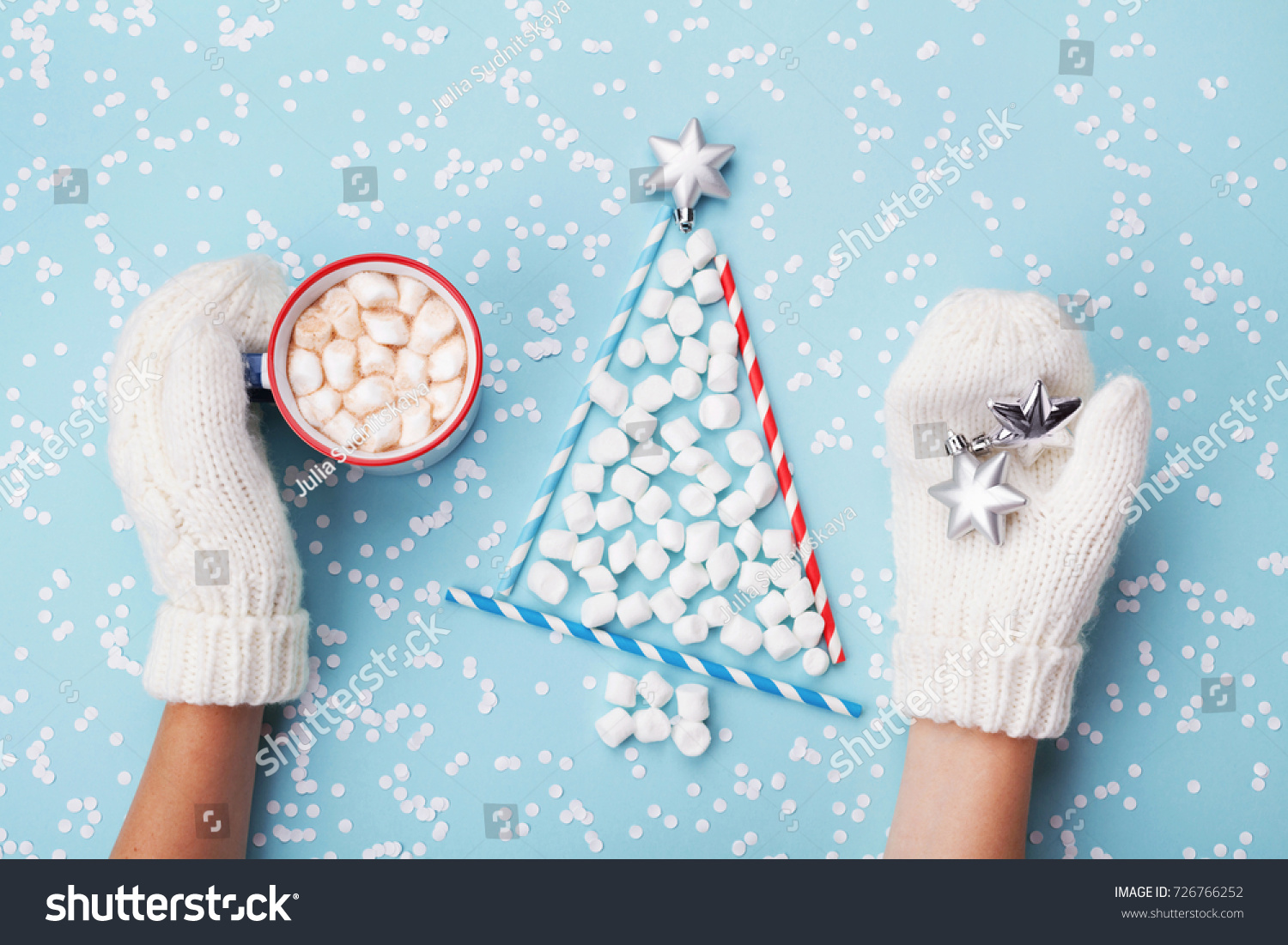 Woman hand in mitten hold cup of hot cocoa or chocolate and christmas fir tree made of marshmallow on turquoise winter background top view. Flat lay. Holiday celebration concept.
