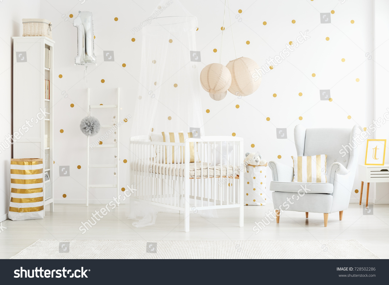 Decor pillow on grey armchair in bright newborn baby's interior with lanterns above bed
