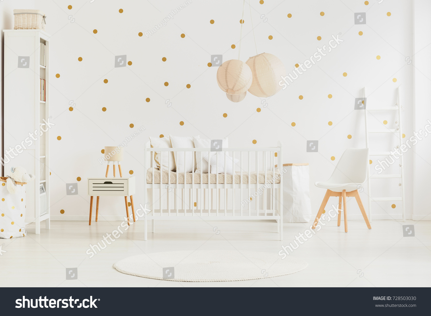 Pastel lanterns above newborn baby's bed in bright bedroom with white chair and cabinet