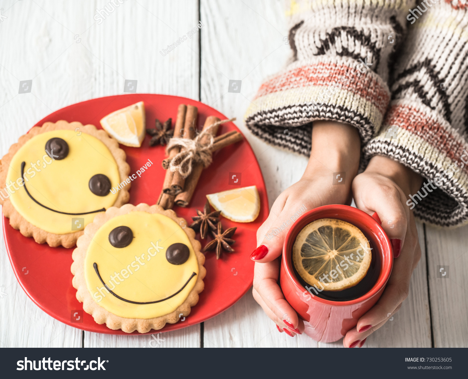 red Cup of hot tea with lemon in hands of the girl in the sweater on a white wooden background red and a plate of cookies the concept of hot drinks
