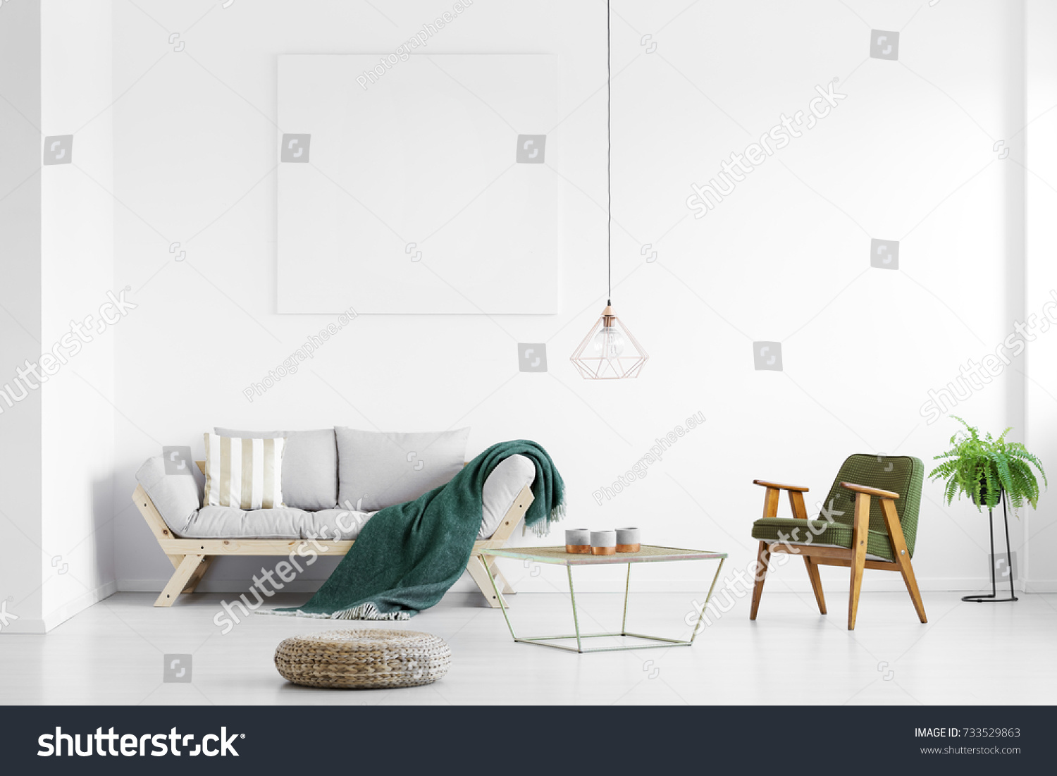 Dark green blanket thrown on grey sofa in bright living room with empty poster and armchair