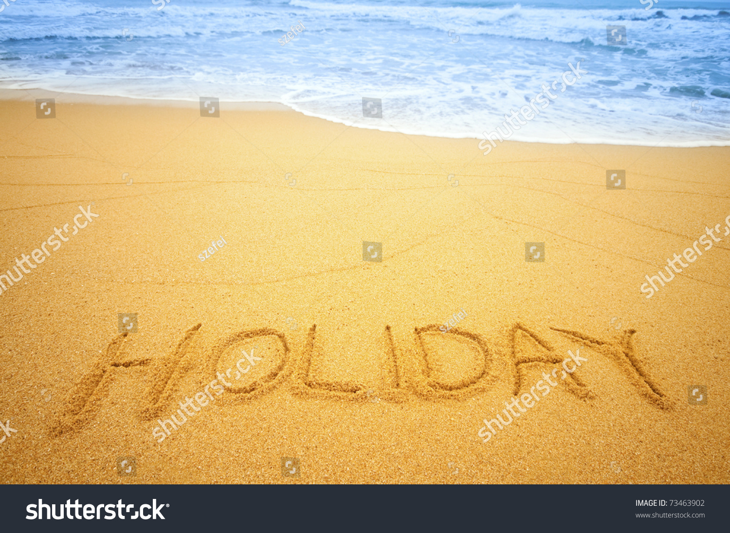 "Holiday" written in the sand on the beach blue waves in the background