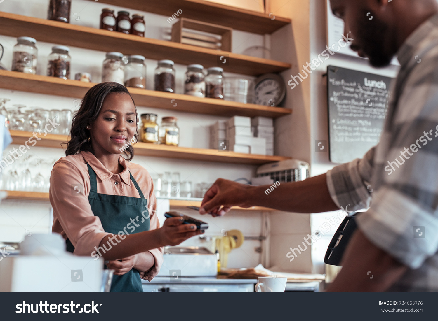 Customer using a bank card and nfs technology to pay a barista for a purchase at a cafe