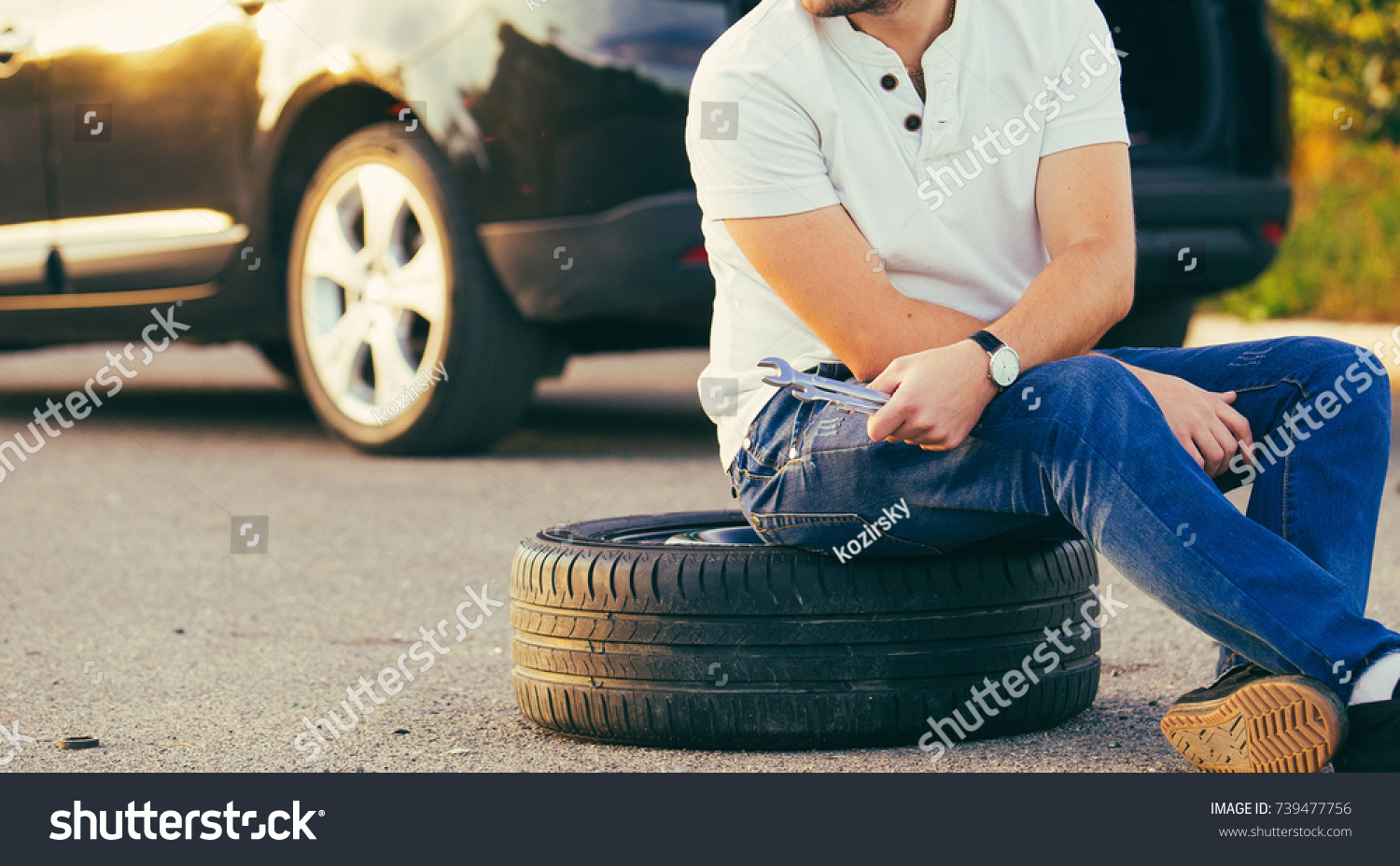 Sad and depressed man sitting near car with punctured tire