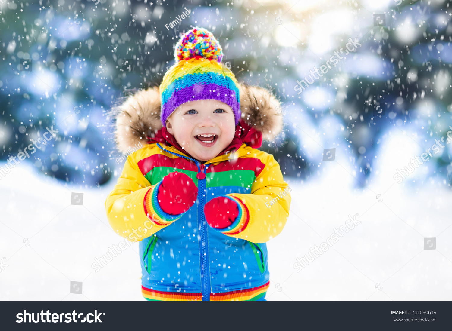 Child playing with snow in winter. Little boy in colorful jacket and knitted hat catching snowflakes in winter park on Christmas. Kids play and jump in snowy forest. Children catch snow flakes