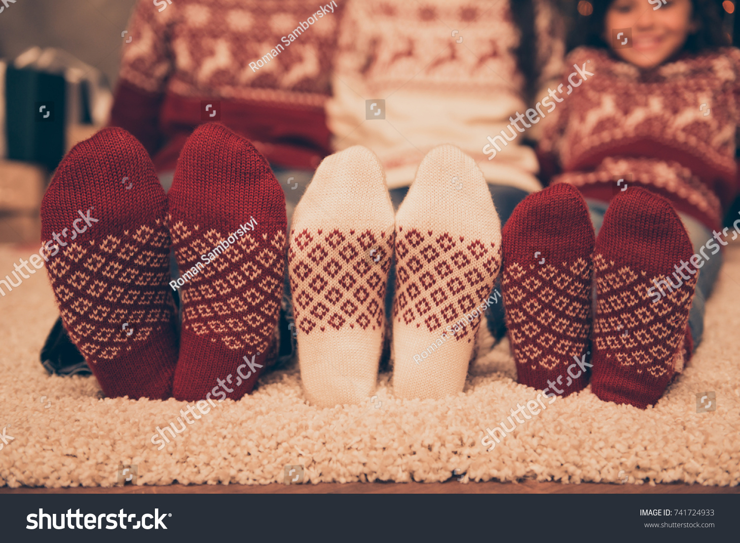 Close up cropped low angle of focus on three pairs of feet of festive husband and wife baby girl sitting down on floor winter december feast x mas noel at coziness in socks