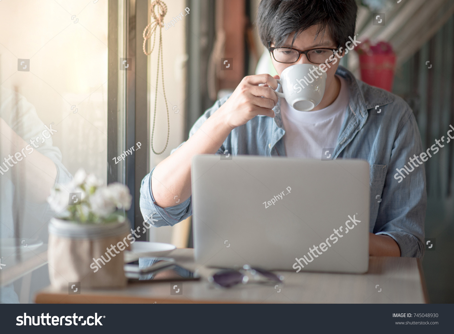 Young Asian happy man using laptop computer during coffee time in cafe casual lifestyle in freelance lifestyle or digital nomad concepts