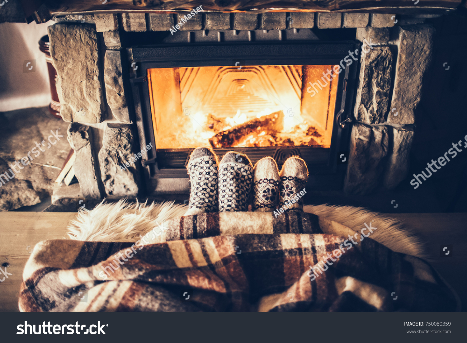 Feet in woollen socks by the Christmas fireplace. Couple sitting under the blanket relaxes by warm fire and warming up their feet in woollen socks. Winter and Christmas holidays concept.
