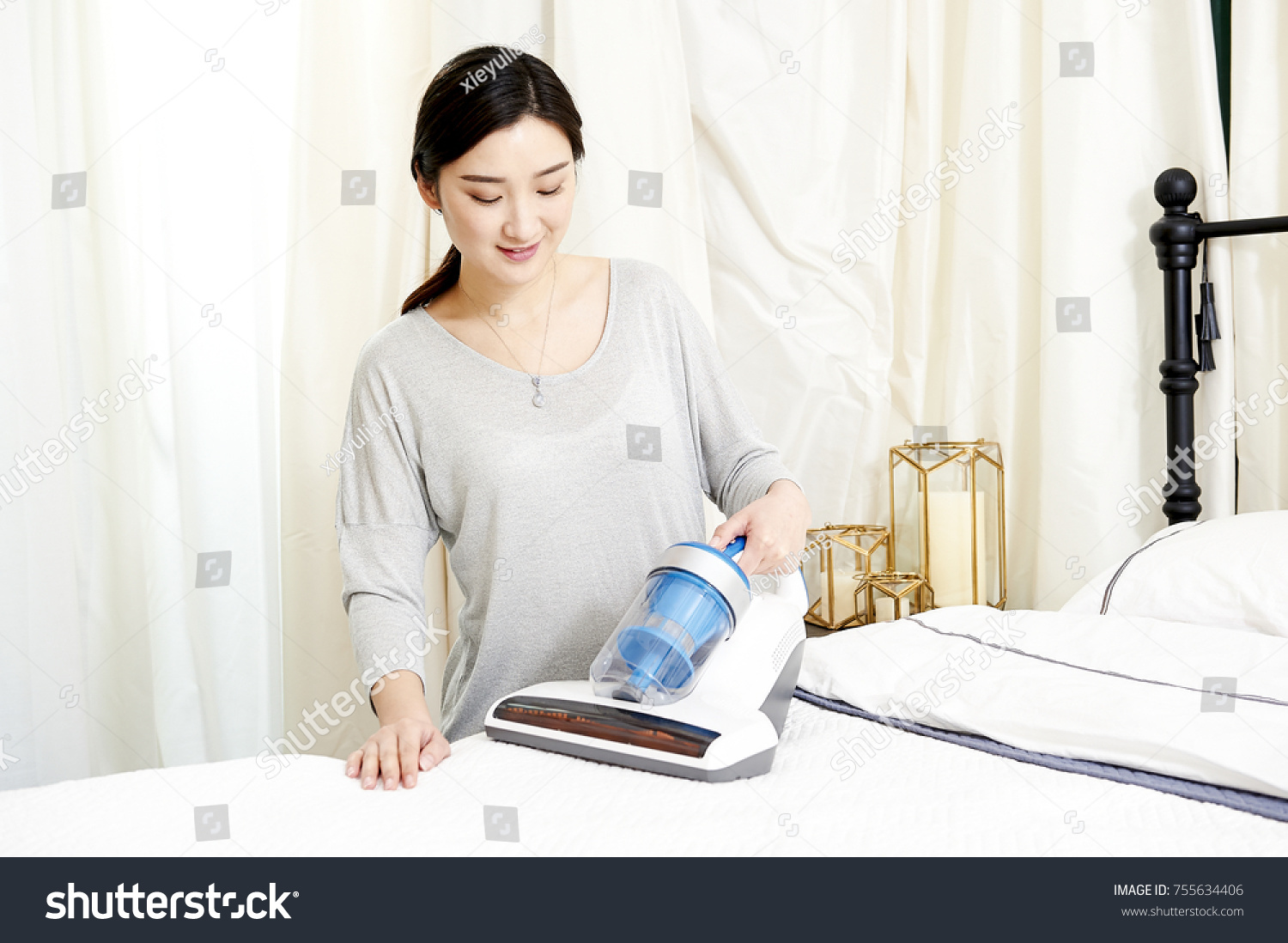 Young Japanese woman knelt in bed using a vacuum cleaner to clean bedding mites