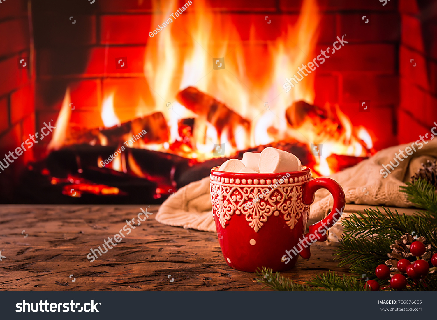 Mug of hot chocolate or coffee with marshmallows in a red mug on vintage wood table in front of Fireplace as a background. Christmas or winter warming drink.