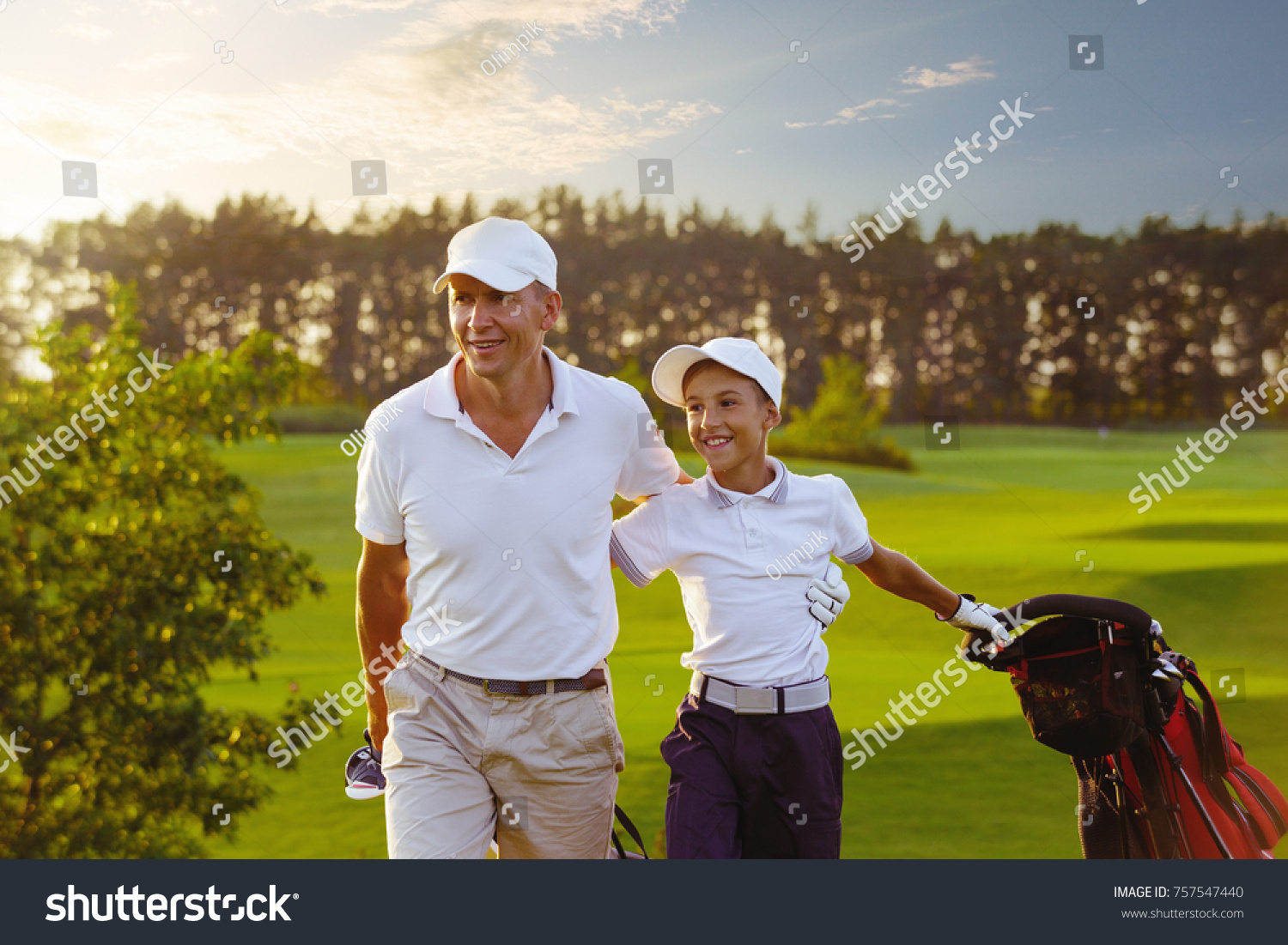 Happy man with his son golfers walking on perfect golf course at summer evening