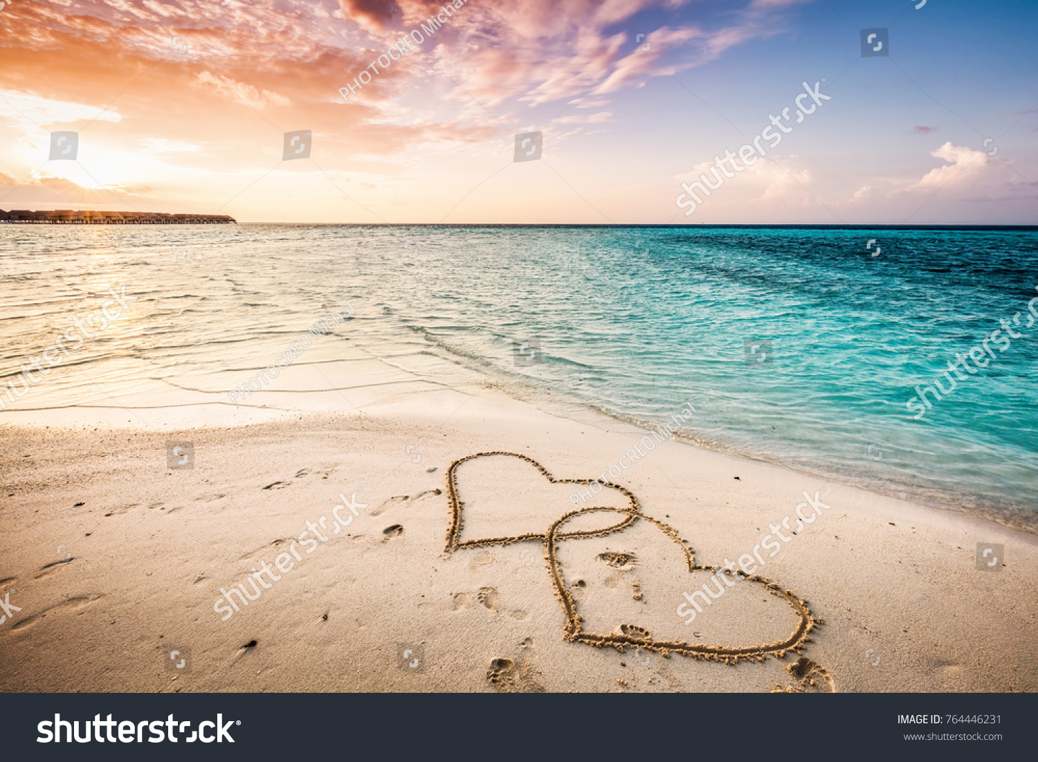 Two hearts drawn on a sandy beach by the sea. Sunset view. Love symbol.
