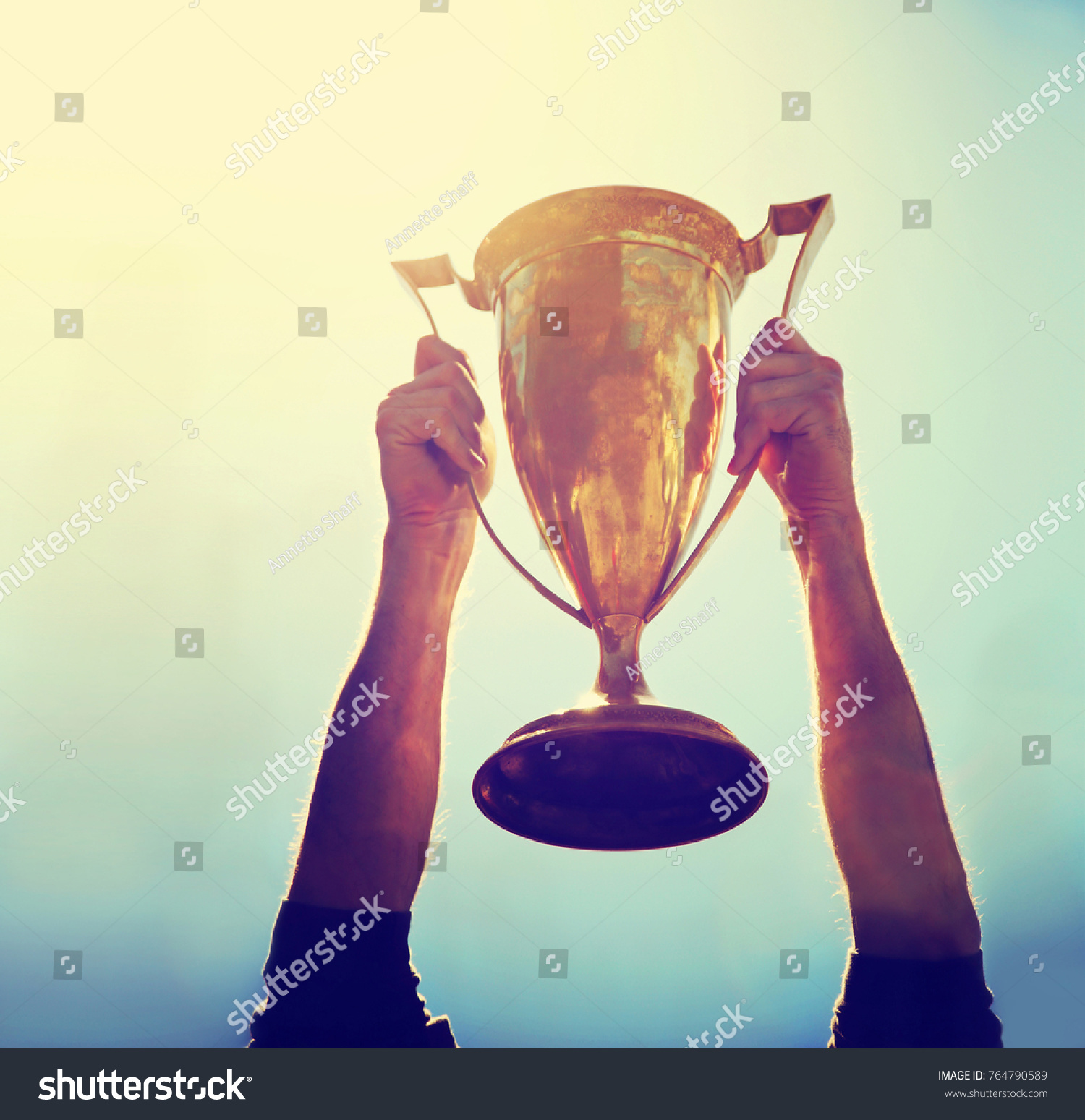 a man holding up a gold trophy cup as a winner in a competition toned with a retro vintage instagram filter effect app or action (SHALLOW DOF on writing)