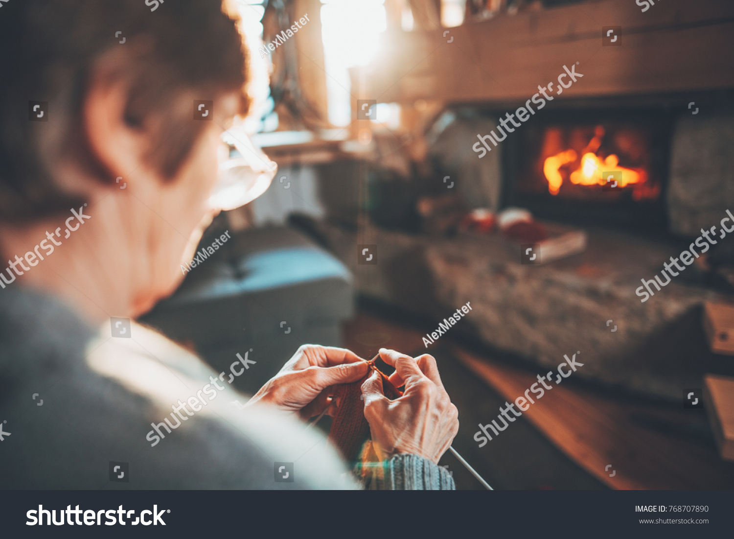 Senior woman hands knitting by the fireplace. Unrecognisable grandmother relaxes by warm fire making handmade gifts for her family. Cozy atmosphere. Winter and Christmas holidays concept.