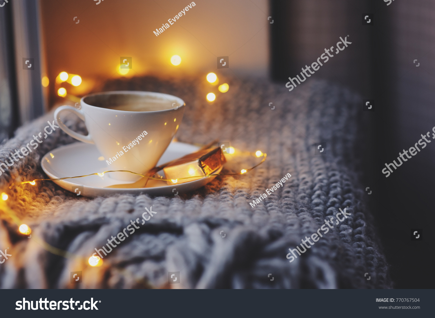 cozy winter or autumn morning at home. Hot coffee with gold metallic spoon warm blanket garland and candle lights swedish hygge concept.