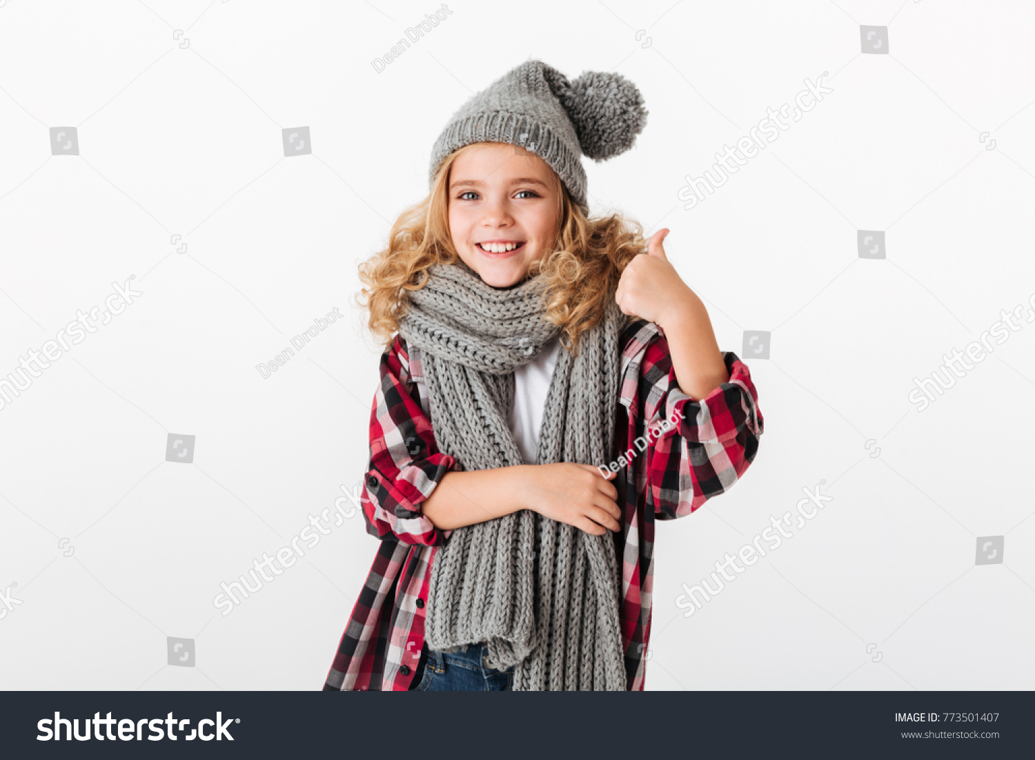 Portrait of a smiling little girl dressed in winter hat and scarf showing thumbs up isolated over white background