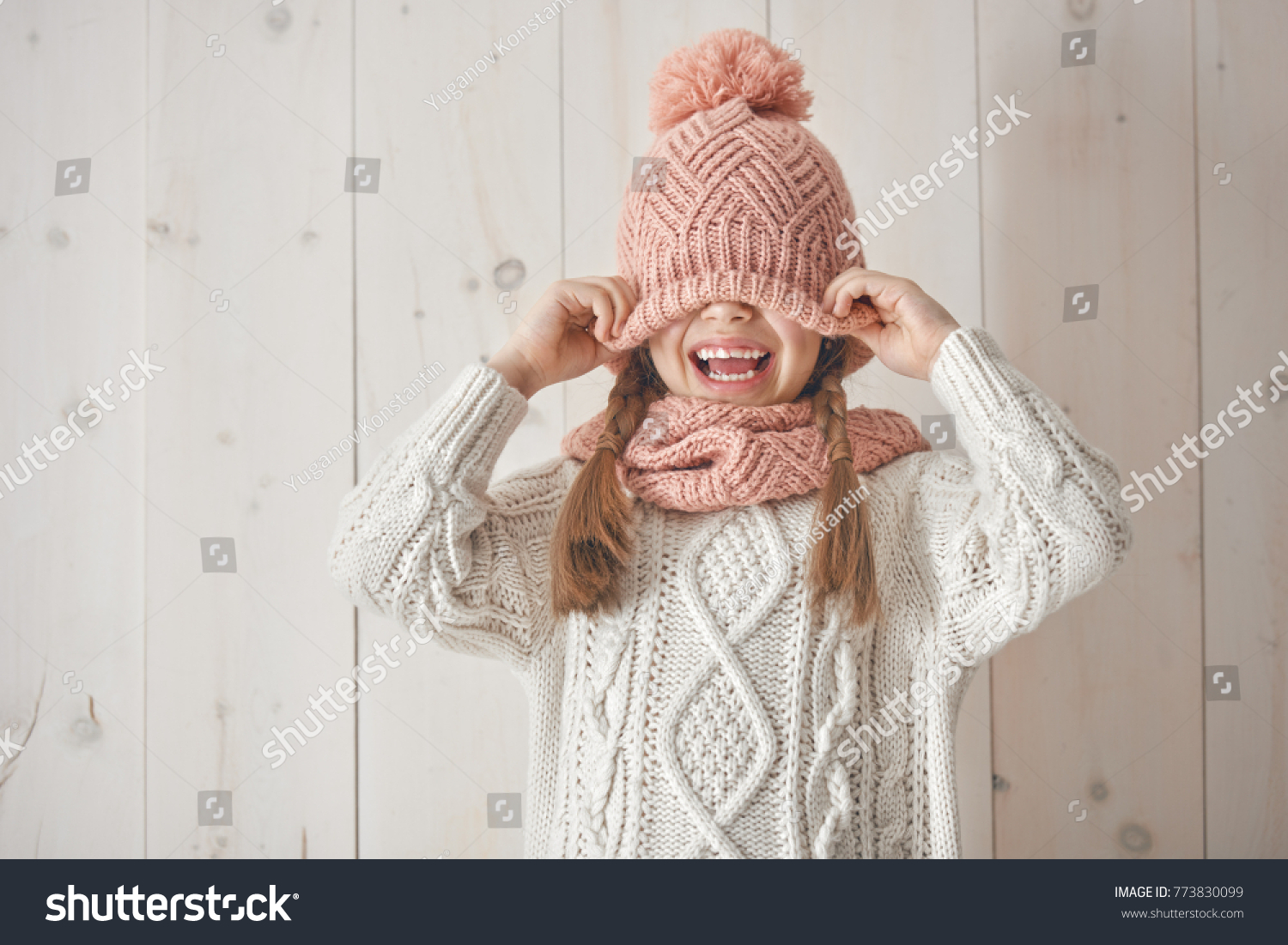 Winter portrait of happy little girl wearing knitted hat scarf and sweater. Child on white wooden background. Fashion concept.