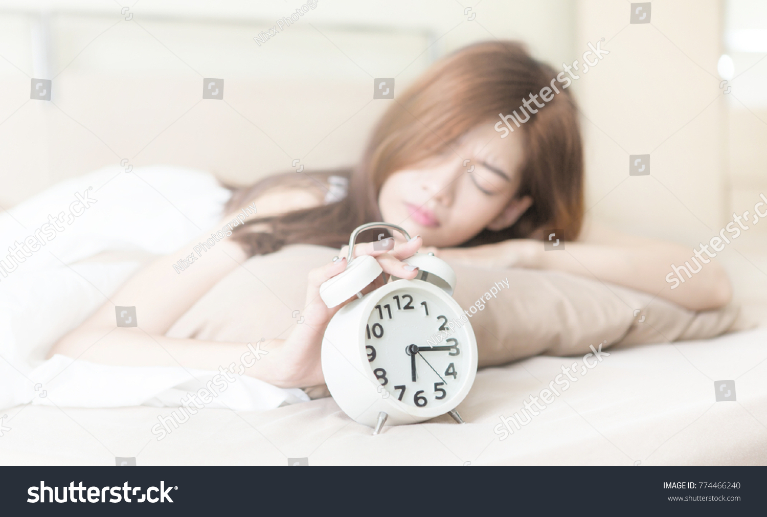 Young beautiful tired and lazy woman try to waking up and turning off the alarm clock