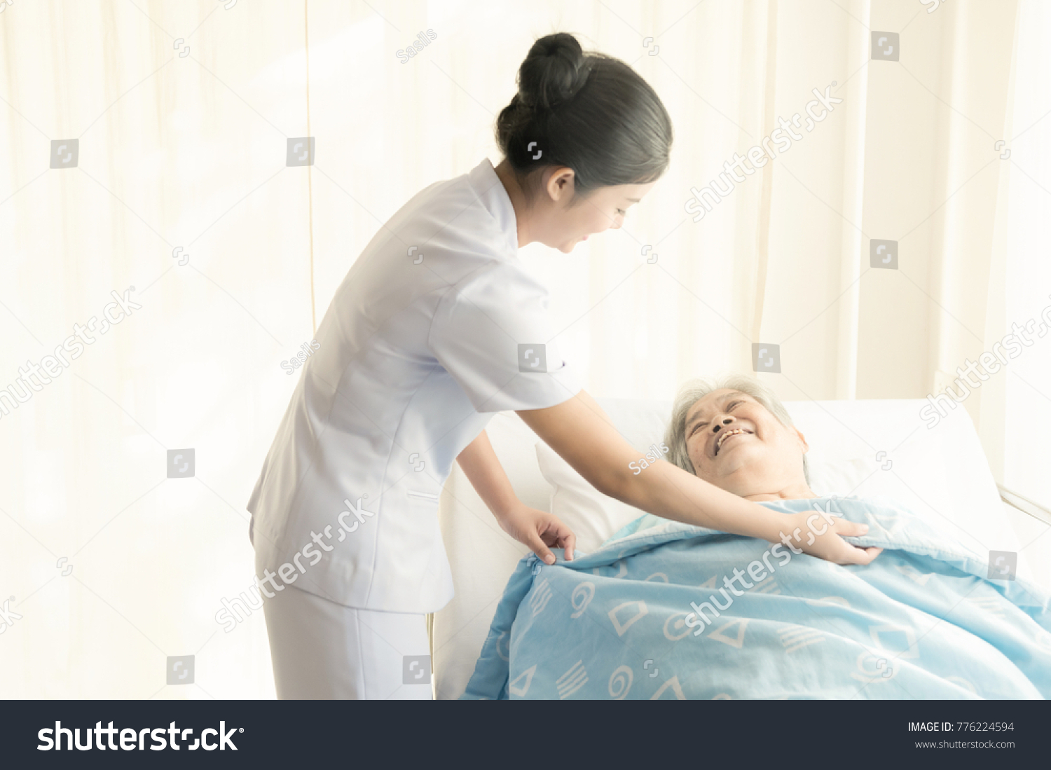 Nurse with patient. Routine health check and putting elderly patient to bed. Female nurse with senior chinese woman.