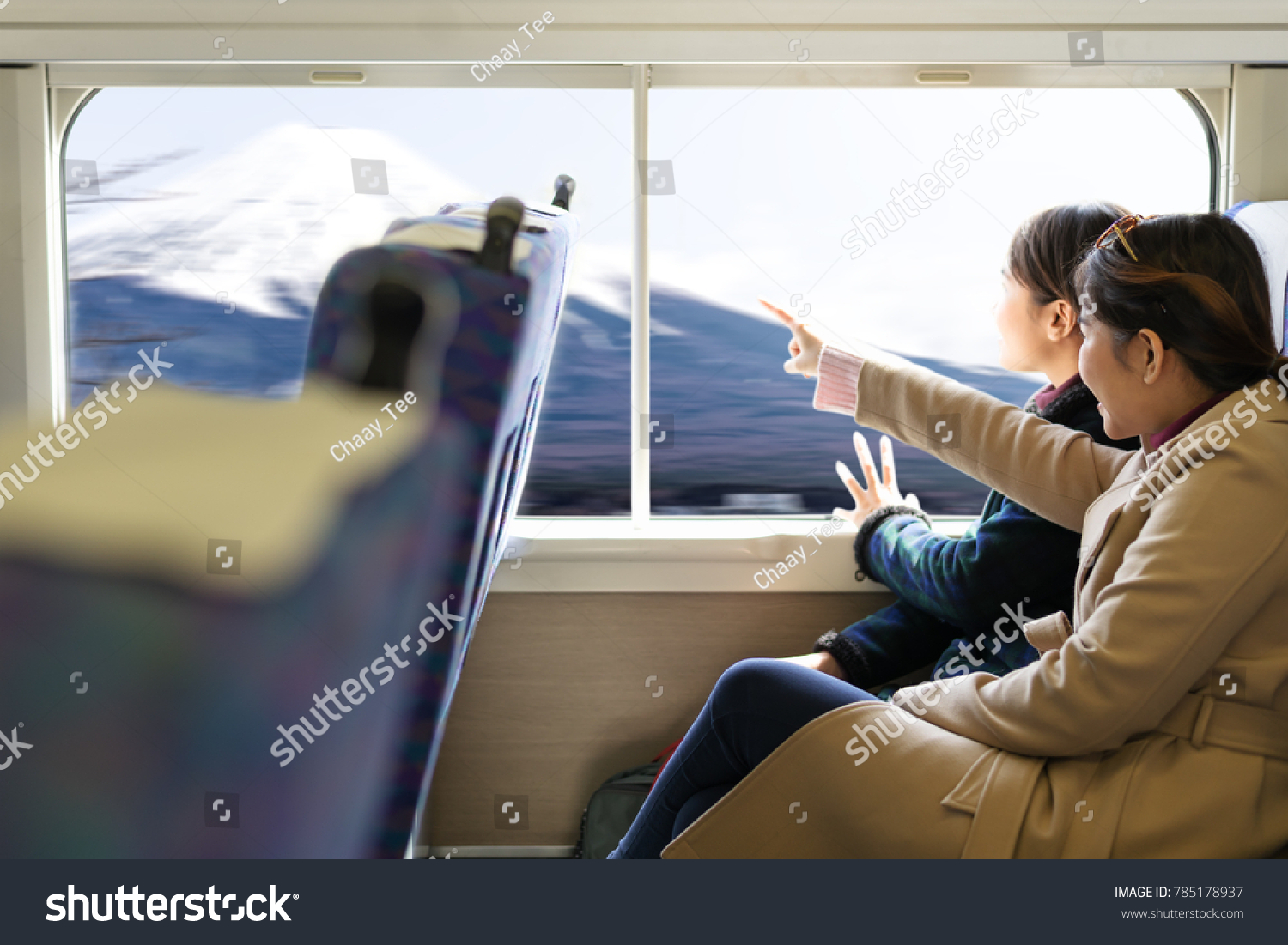 Two cute asian traveler woman traveling by train sitting near window and looking outside with mountain Fuji view. Feeling chilling and enjoy travel.