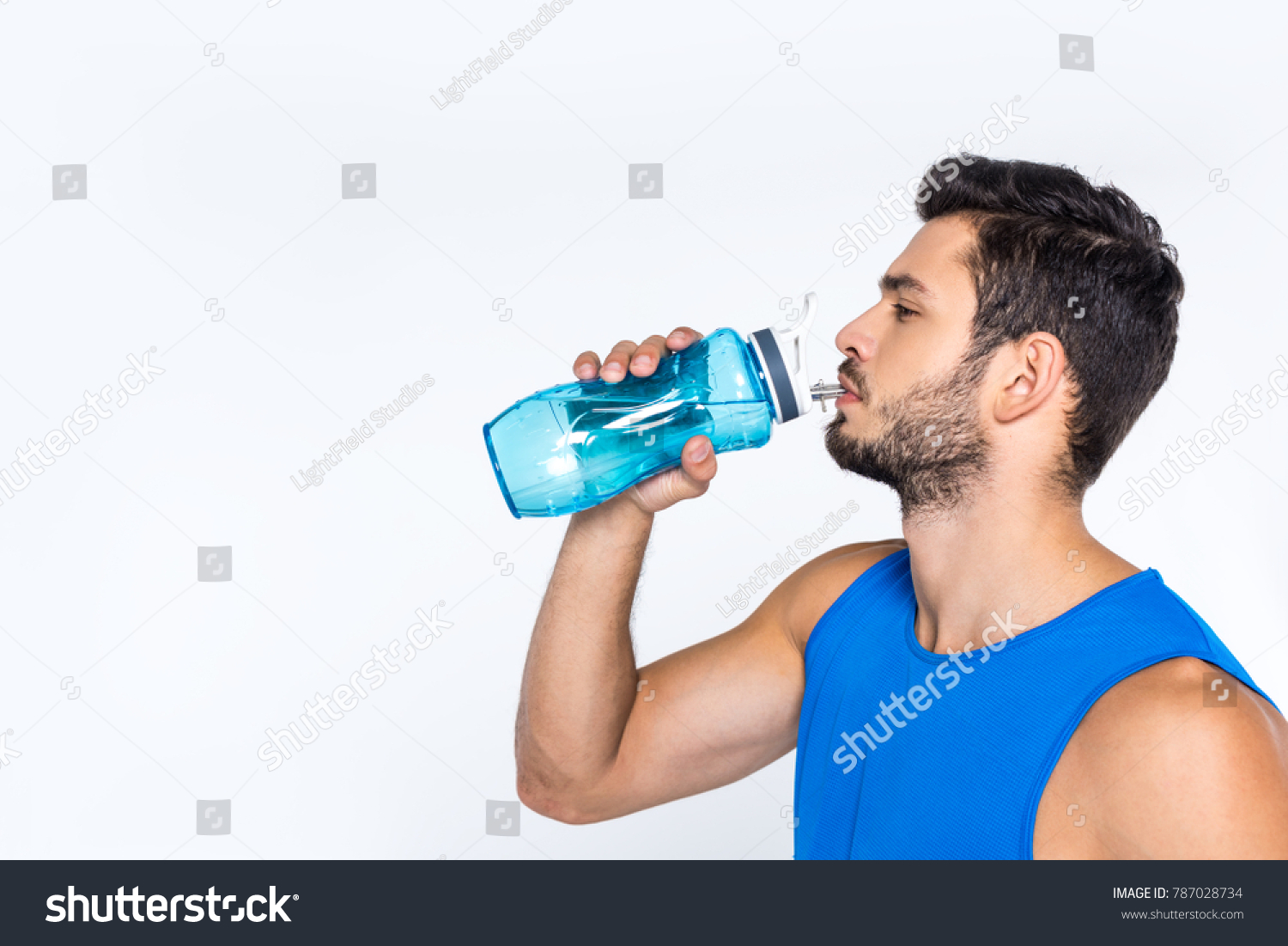 side view of sporty young man drinking water from fitness bottle isolated on white
