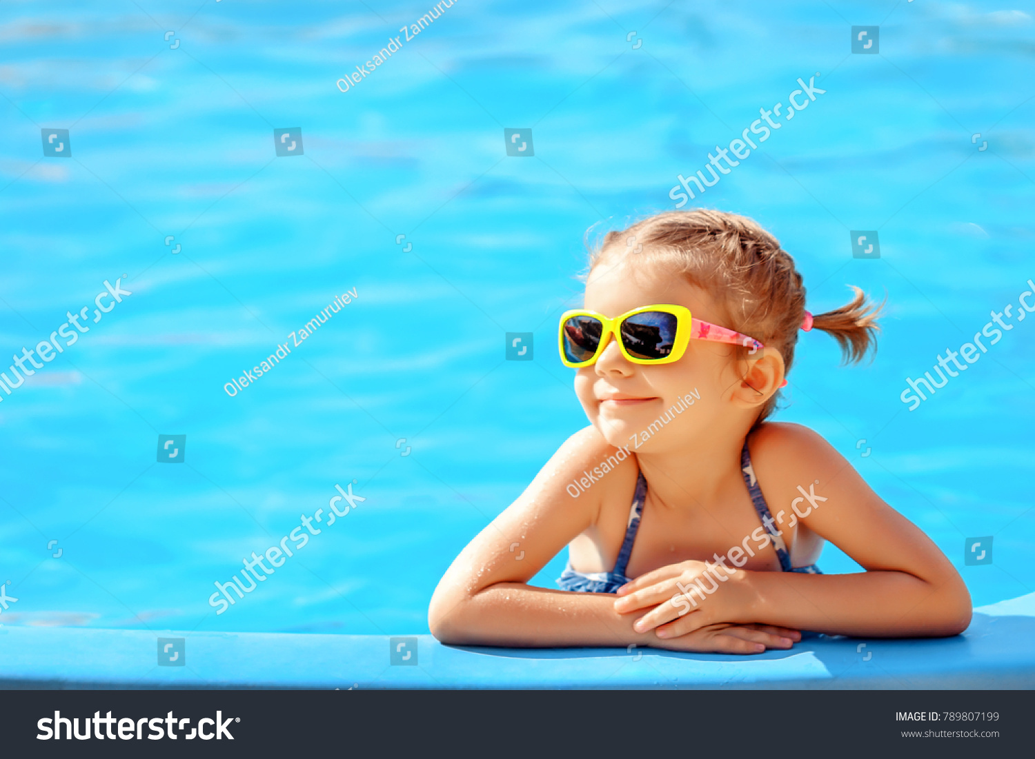 Smiling cute little girl in sunglasses in pool in sunny day.