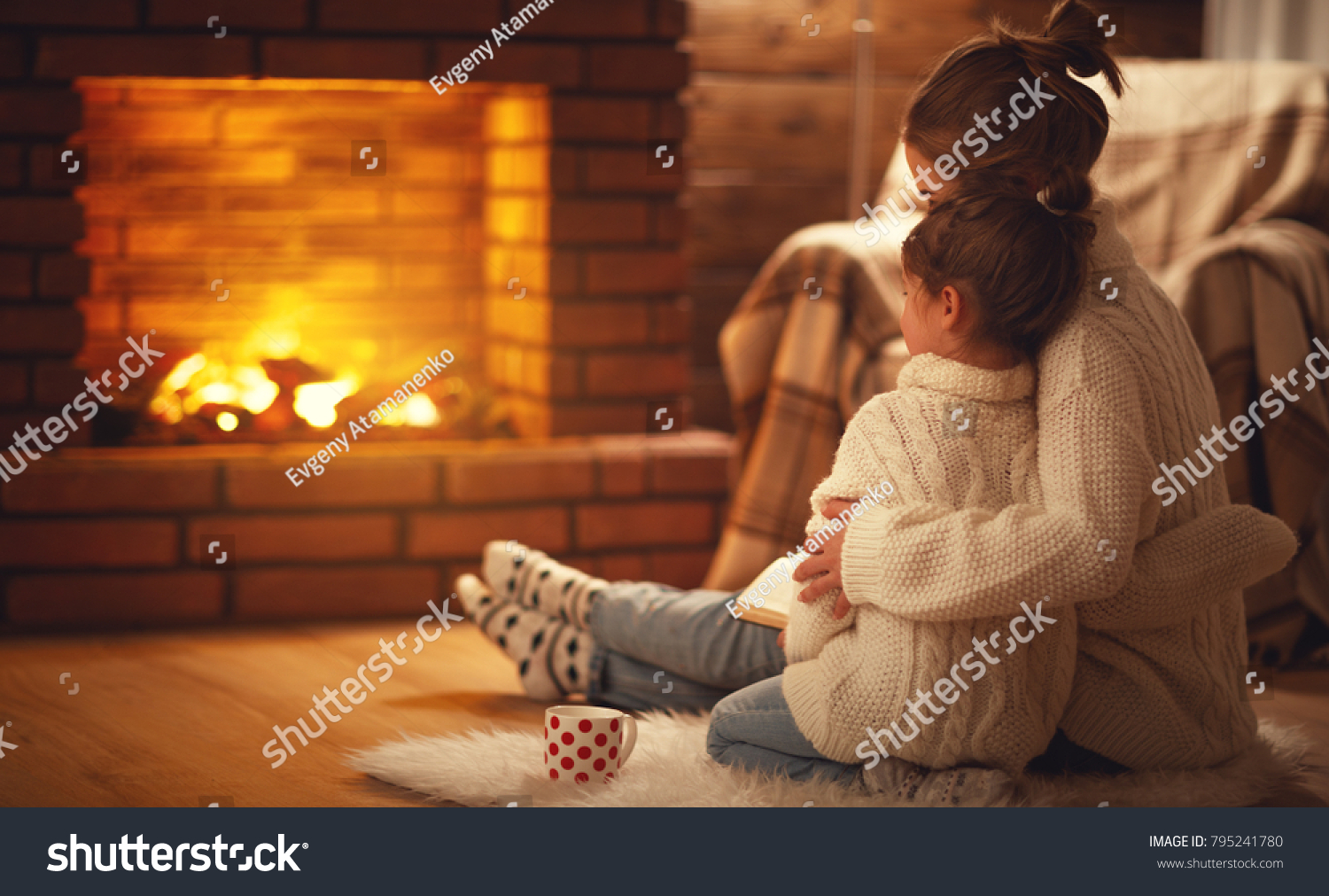family mother and child daughter hugs and warm on winter evening by fireplace