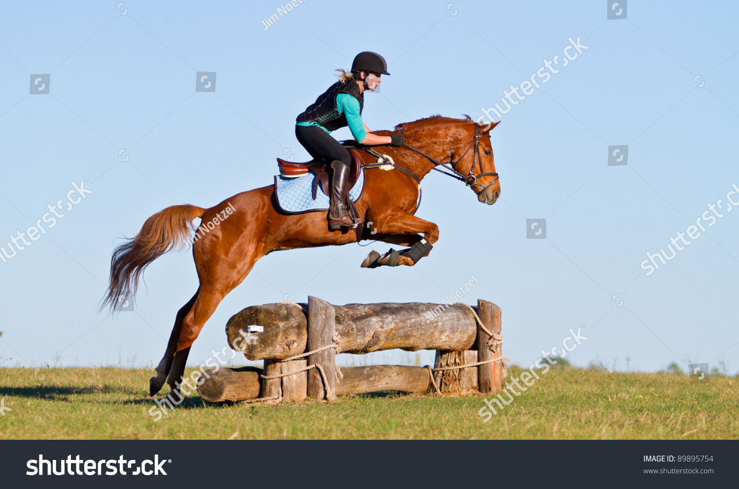 woman jumping horse over log obstacle on cross country course