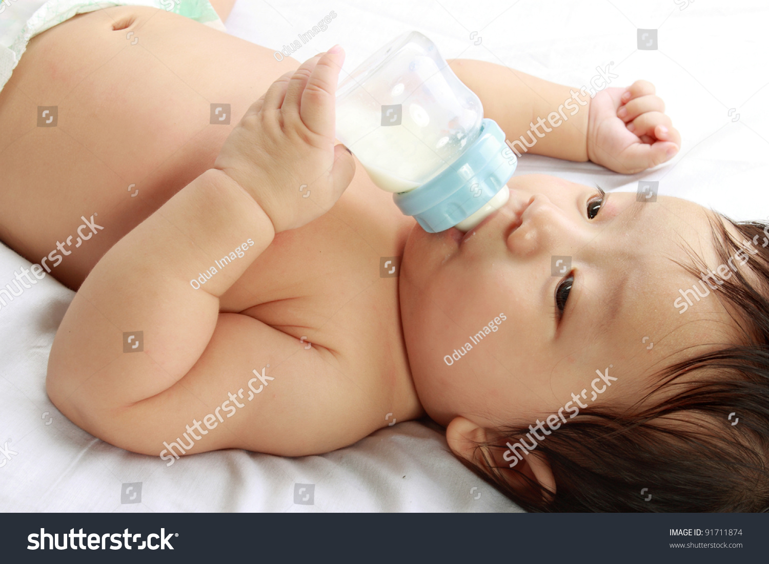 little baby boy drinks milk from bottle holded by him self  lying on bed