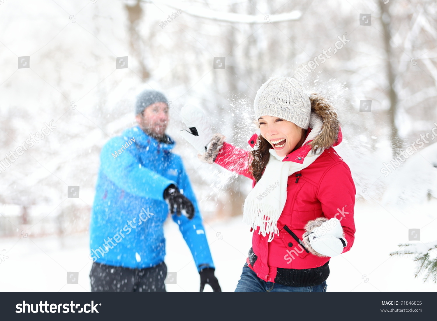 Snowball fight. Winter couple having fun playing in snow outdoors. Young joyful happy multi-racial couple.